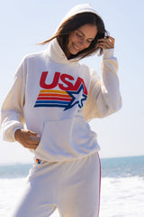 Person wearing a white hoodie with 'USA' and star design on a beach