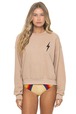 Woman wearing a beige sweatshirt with a black lightning bolt design and colorful underwear on a white background